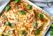 A sheet pan of pesto lasagna, a bowl of parmesan cheese, and some basil leaves.