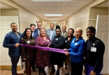 Alpha House East Expands Shelter Options for Families in Need Group of racially diverse people in a hallway with an African American woman in a black dress holding the ceremonial "grand opening" scissors, cutting a purple ribbon.